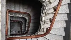 View of the 4 flights of stairs from the top; stairs in a spiral-like shape; wood rail up until the hostel.