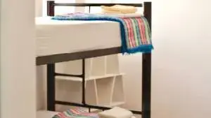 Bunk beds in a dorm room in the hostel; simple, white sheets and colorful woven cover.